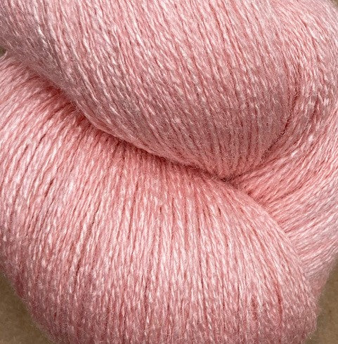 A close-up of a skein of JaggerSpun Zephyr Wool-Silk 2/18 Yarn in a pale pink hue. The fibers appear soft and slightly shiny, creating a delicate texture. This luxurious yarn from Jagger Brothers, Inc., made from premium silk and wool, is loosely twisted into a skein, showcasing its uniform color and smoothness.