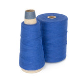 Two spools of blue thread are shown. The spool on the left is tapered and taller, wrapped with blue thread with a gray top. The spool on the right is shorter and wider, fully wrapped with blue thread. Both are standing upright on a white background, perfect for your next project with Maurice Brassard's 8/2 Cottolin Organic Yarn | Mini-Cone.