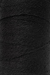 A close-up of a spool of Maurice Brassard's Cotton Bouclé Yarn in black, showcasing its texture and tightly wound fibers. The yarn appears slightly fuzzy, indicating a soft cotton material. The image highlights the uniformity and consistency of the winding, making it perfect for weaving projects.