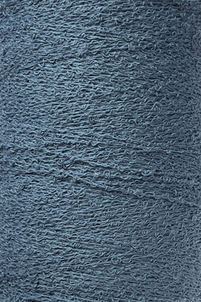 A close-up image of a spool of Maurice Brassard Cotton Bouclé Yarn. The yarn, tightly wound on a tube, exhibits visible fibers and slight irregularities that enhance its textured appearance. The muted, cool blue color of the yarn suggests a soft and cozy material ideal for creating Maurice Brassard weavings.