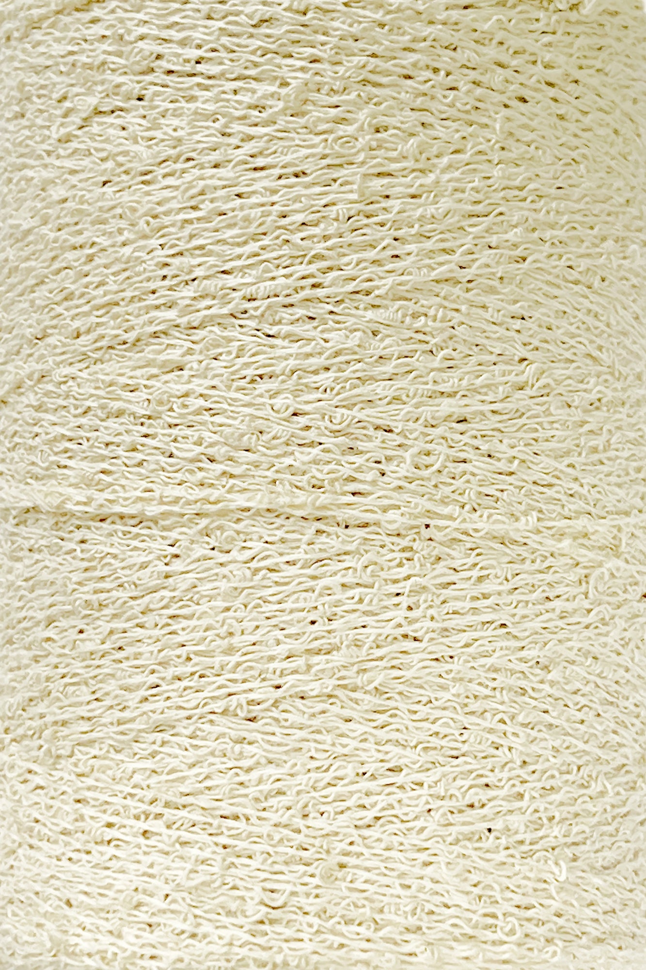 A close-up image of a large spool of cream-colored yarn. The yarn texture appears soft and slightly twisted, with visible fibers intertwined uniformly throughout the spool. Featuring what appears to be Cotton Bouclé Yarn in a Tube by Maurice Brassard, the image captures the intricate details and smoothness of the yarn's surface.