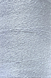 Close-up image of a spool of Maurice Brassard's Cotton Bouclé Yarn. The white thread appears tightly wound, showcasing a slightly textured, curly pattern characteristic of Cotton Bouclé. The overall impression is clean and uniform with a smooth yet intricate surface.