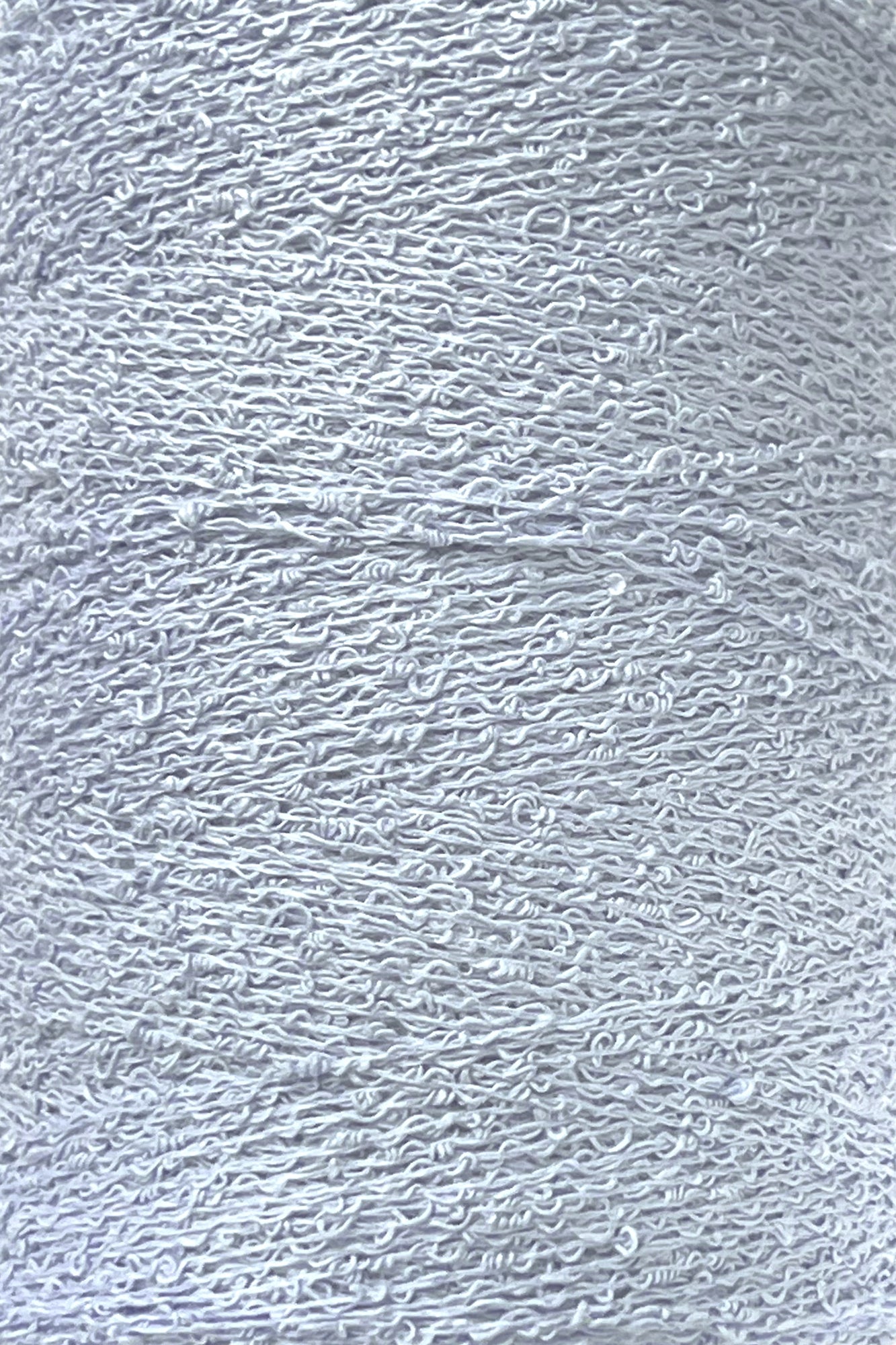 Close-up image of a spool of Maurice Brassard's Cotton Bouclé Yarn. The white thread appears tightly wound, showcasing a slightly textured, curly pattern characteristic of Cotton Bouclé. The overall impression is clean and uniform with a smooth yet intricate surface.