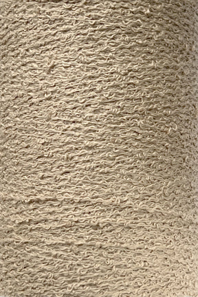 Close-up of a large spool of Maurice Brassard's Cotton Bouclé Yarn. The tightly wound, beige yarn exhibits a slightly rough, uneven texture indicative of natural fiber. The uniform color and distinct texture make it well-suited for knitting or weaving projects.