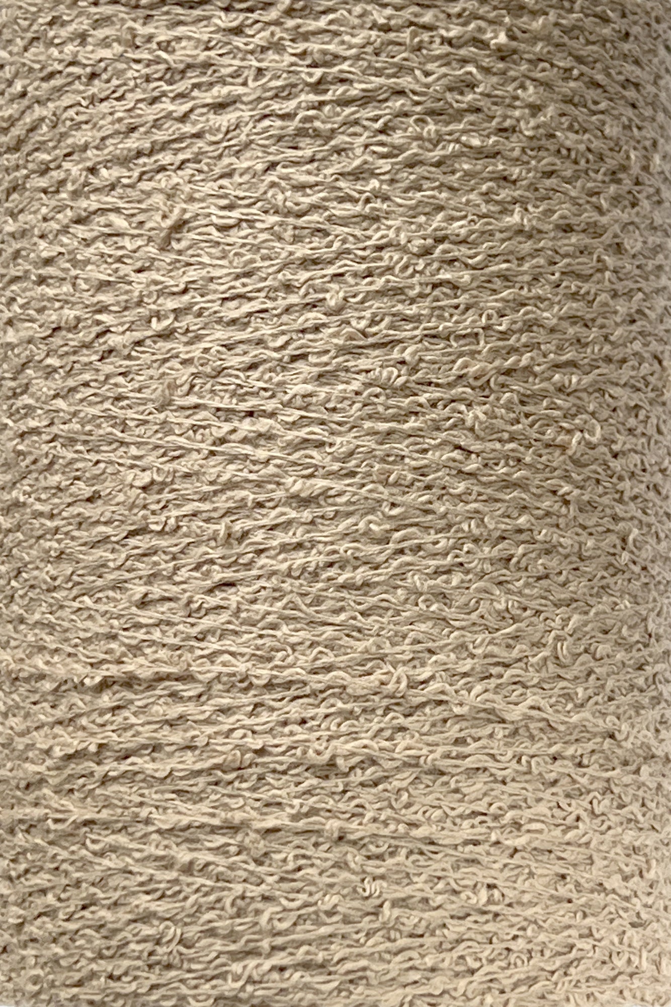 Close-up image of a large spool of Cotton Bouclé Yarn | Mini-Cone by Maurice Brassard. The fibers, made from 100% cotton bouclé, are tightly wound, creating an intricate, rough surface with numerous small loops and twists visible throughout the material—perfect for weaving cotton projects inspired by Maurice Brassard's designs.