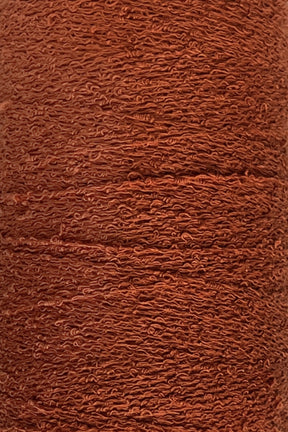 Close-up image of a spool of reddish-brown yarn with a textured, slightly wavy appearance. The densely wound Maurice Brassard Cotton Bouclé Yarn | Tube showcases intricate and uniform layers throughout.