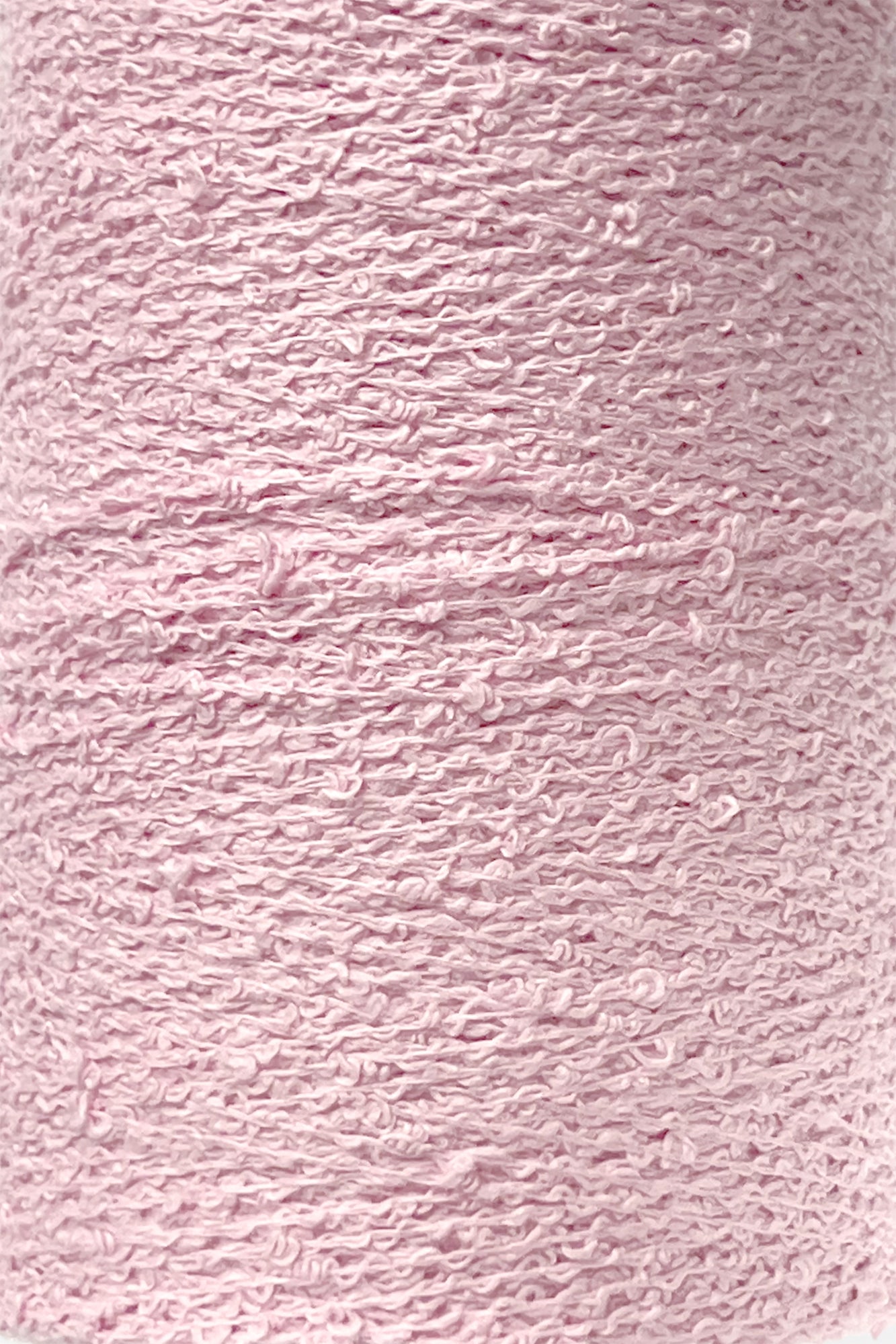 A close-up image of Maurice Brassard's Cotton Bouclé Yarn in light pink. The yarn features a textured, somewhat bumpy surface and is tightly wound around the tube. Its overall appearance is soft and pastel-colored, making it ideal for delicate cotton knitting or weaving projects.