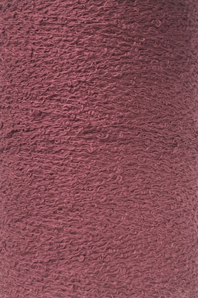 Close-up shot of a large cone of maroon-colored Maurice Brassard Cotton Bouclé Yarn. The yarn appears to be tightly wound with a slightly rough surface, and the fibers have a uniform color with a texture that hints at a blend of materials.