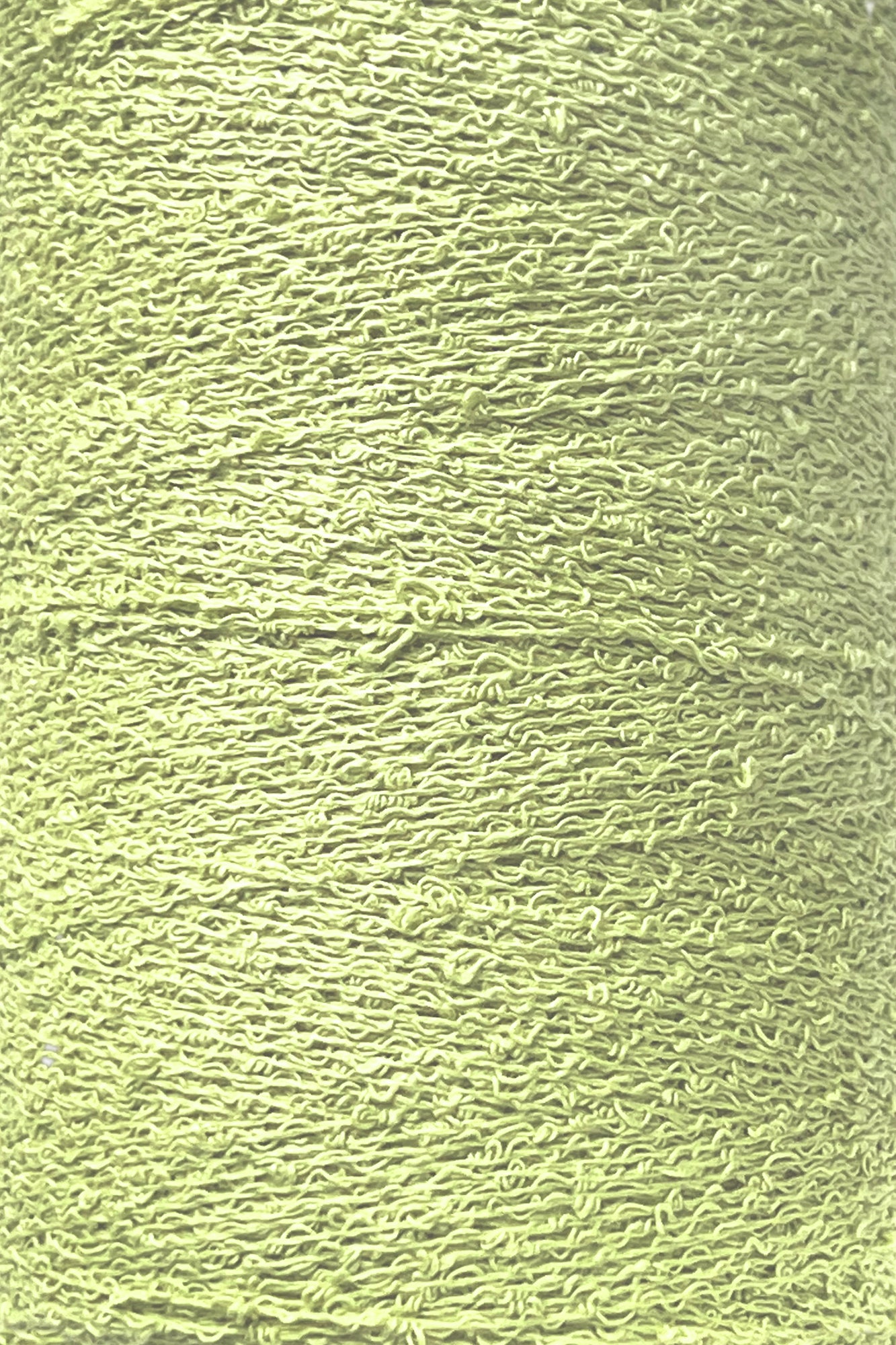 Close-up image of a spool of Maurice Brassard's Cotton Bouclé Yarn in light green. The yarn has a slightly uneven and loopy texture, reminiscent of classic bouclé, creating an intricate pattern across the surface of the tube.