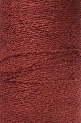 Close-up of a spool of Maurice Brassard Cotton Bouclé Yarn | Tube, featuring its textured, reddish-brown fibers with a slightly rough and uneven surface. The yarn boasts a semi-matte finish and appears tightly wound, showcasing visible twists and loops in the strands.