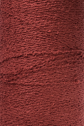 Close-up of a spool of Maurice Brassard Cotton Bouclé Yarn | Tube, featuring its textured, reddish-brown fibers with a slightly rough and uneven surface. The yarn boasts a semi-matte finish and appears tightly wound, showcasing visible twists and loops in the strands.