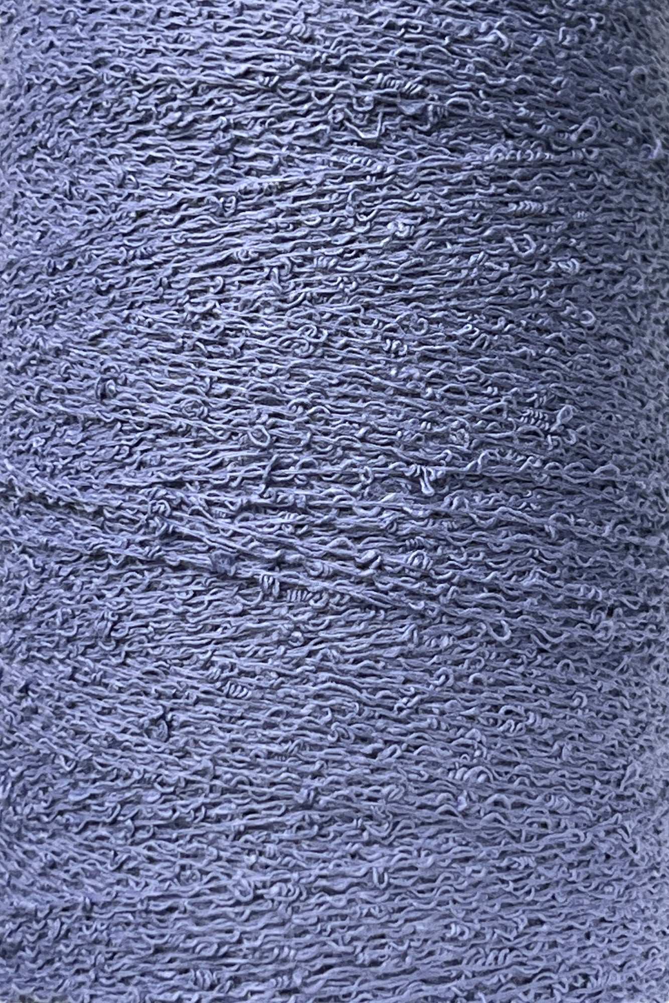 A close-up image of a grey textured surface, resembling tightly coiled and looped threads like those in Maurice Brassard's Cotton Bouclé Yarn. The intricate pattern creates a sense of depth and complexity across the entire view.