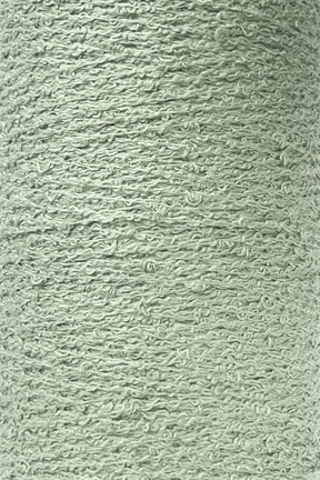 A close-up image of a spool of Maurice Brassard's Cotton Bouclé Yarn | Tube in light grey-green. The yarn displays a slightly rough and textured appearance, with visible individual fibers and small loops throughout. The color is consistently spread across the entire surface, making it ideal for various cotton weaving projects.