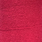 Close-up image of a textured surface in a deep red color. The texture, resembling Maurice Brassard's Cotton Bouclé Yarn | Tube, features numerous small, swirling patterns that give it a slightly rough and intricate appearance. Perfect for weaving cotton enthusiasts seeking unique fabric details.