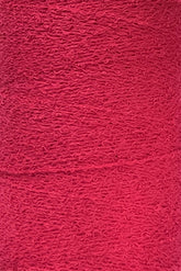 Close-up image of a textured surface in a deep red color. The texture, resembling Maurice Brassard's Cotton Bouclé Yarn | Tube, features numerous small, swirling patterns that give it a slightly rough and intricate appearance. Perfect for weaving cotton enthusiasts seeking unique fabric details.