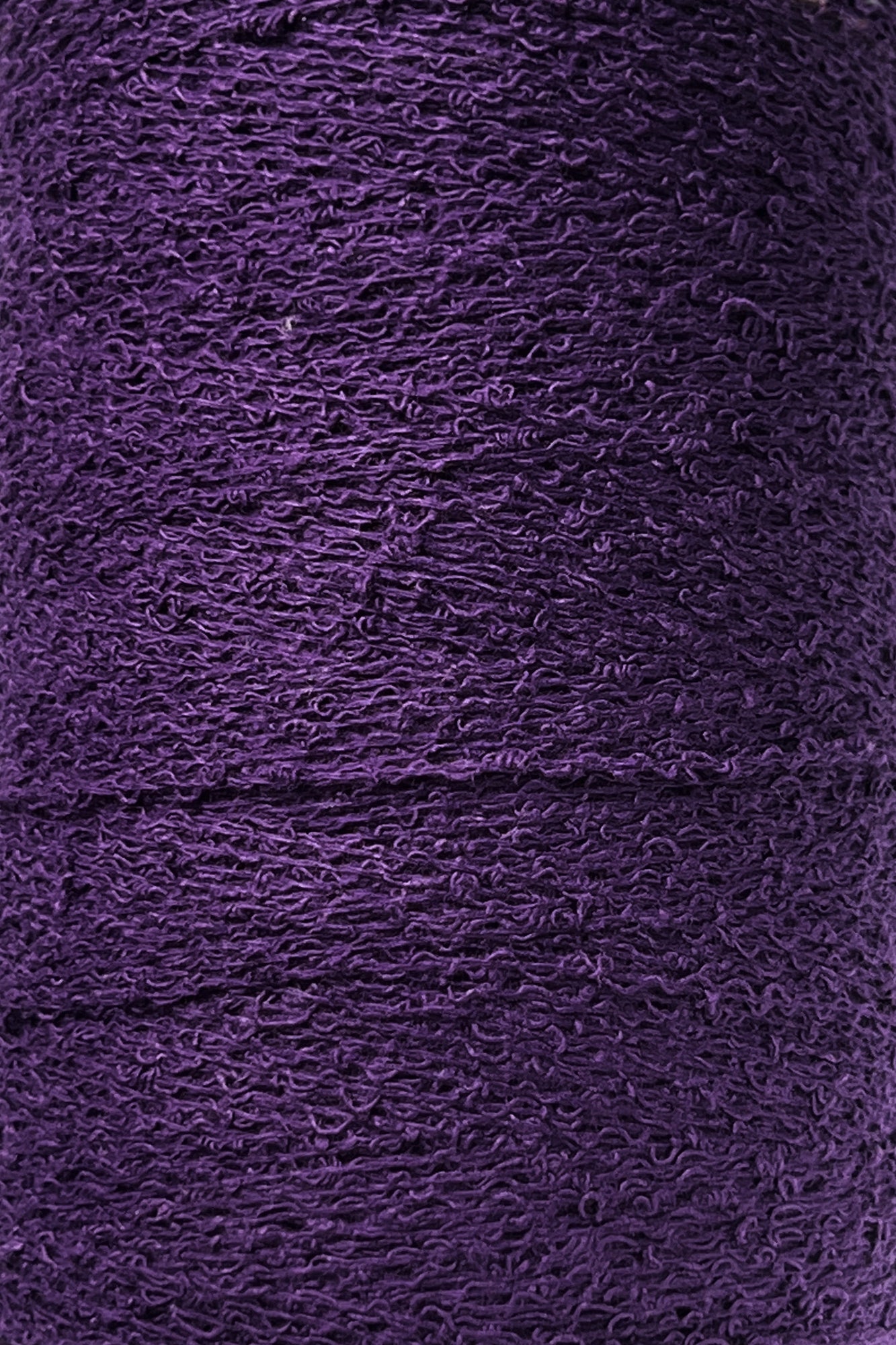 Close-up shot of a tightly wound spool of Maurice Brassard's Cotton Bouclé Yarn in purple. The slightly rough surface of this weaving yarn appears dense, with layers stacked consistently in a continuous pattern.