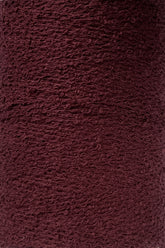 A close-up of a textured, deep burgundy fabric with a slightly rough and uneven surface. The material, likely Maurice Brassard Cotton Bouclé Yarn | Tube, showcases a woven appearance, with visible loops and threads creating a tactile, rich color and intricate pattern.