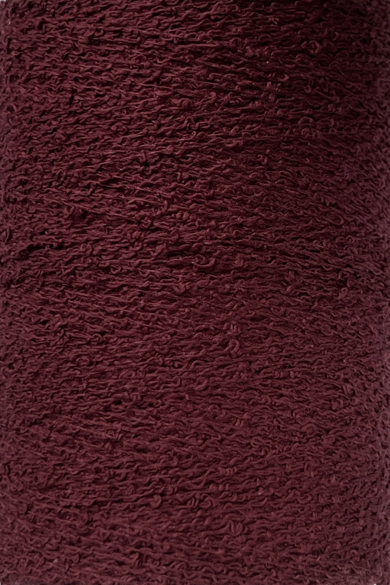 A close-up of a textured, deep burgundy fabric with a slightly rough and uneven surface. The material, likely Maurice Brassard Cotton Bouclé Yarn | Tube, showcases a woven appearance, with visible loops and threads creating a tactile, rich color and intricate pattern.