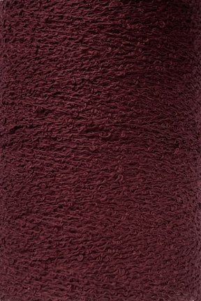 A close-up of a textured, deep burgundy fabric with a slightly rough and uneven surface. The material, likely Maurice Brassard Cotton Bouclé Yarn | Tube, showcases a woven appearance, with visible loops and threads creating a tactile, rich color and intricate pattern.