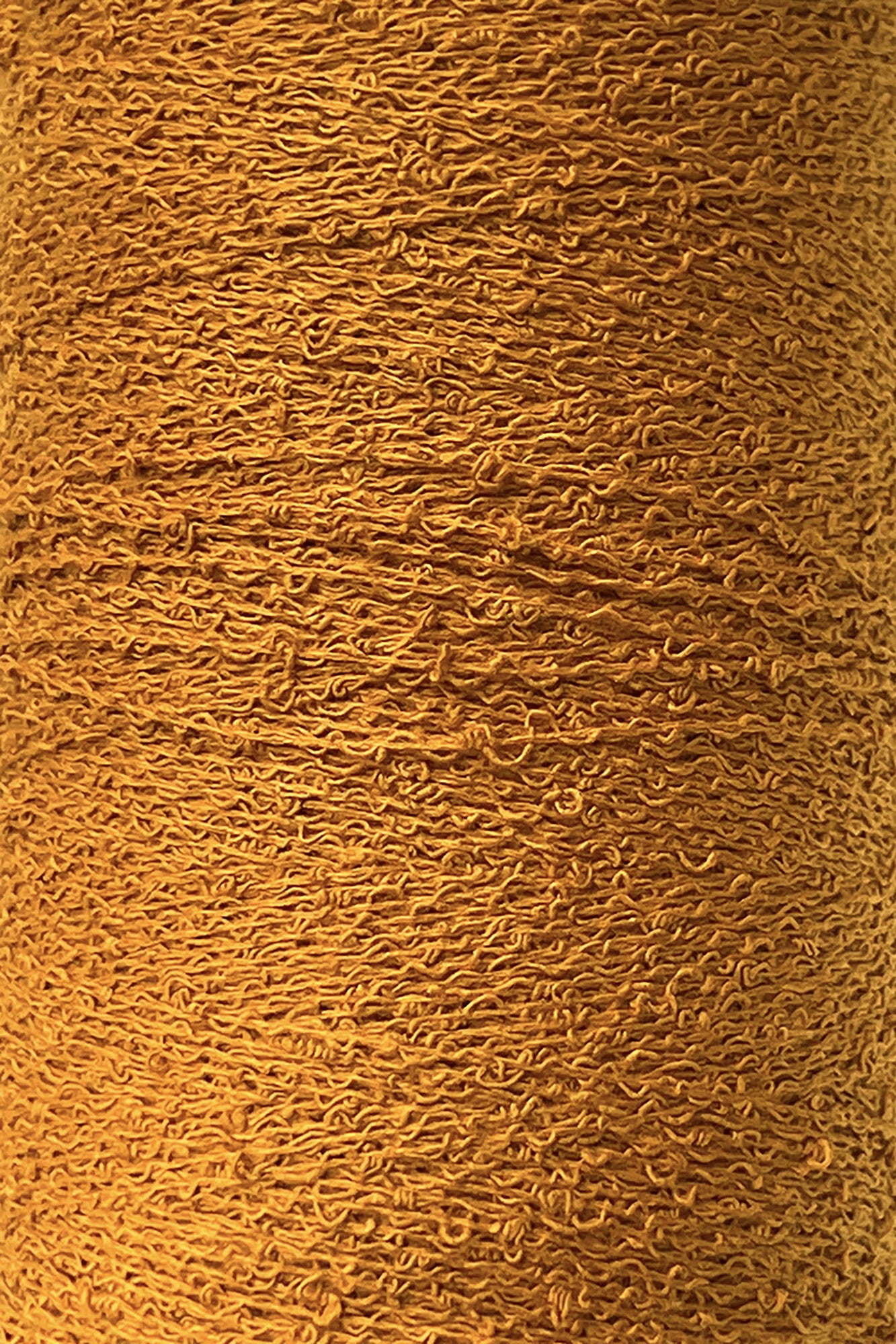 Close-up image of a spool of Maurice Brassard's Cotton Bouclé Yarn in golden yellow, showcasing intricate and tightly wound threads that form a textured pattern. The soft cotton yarn displays slight shade variations due to the lighting and texture, reminiscent of classic weaving cotton.