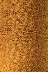 Close-up of a textured, golden-brown fabric roll. The fabric, woven with 100% Cotton Bouclé Yarn | Mini-Cone from Maurice Brassard, features tightly interwoven threads creating intricate patterns with a tactile and slightly rough surface. The color is consistent throughout, emphasizing the detailed craftsmanship.