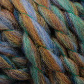 Close-up of thick, multi-colored Bear Creek Yarn by Kraemer twisted together. The yarn features shades of blue, green, and brown, creating a textured, vibrant pattern with visible fibers. The image highlights the intricate details and soft texture of the domestic wool by Kraemer.