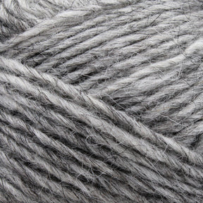 A close-up of Berroco, Inc.'s Léttlopi (Lite Lopi) Icelandic Wool Yarn in gray reveals an intricate blend of light and dark threads intertwined. The soft and fluffy texture makes it ideal for creating durable garments or engaging in colorwork knitting projects.