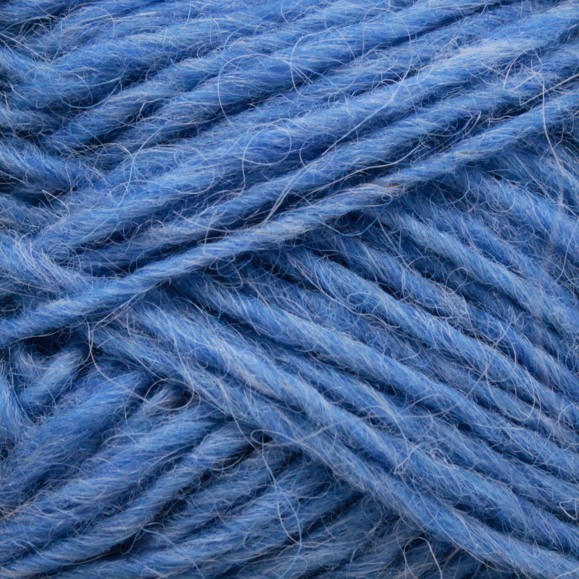 A close-up of Berroco, Inc.'s Léttlopi (Lite Lopi) Icelandic Wool Yarn showcases its soft, fibrous texture with various shades of blue intertwining. The image captures the intricate detail of the yarn's strands, highlighting its fluffy and slightly fuzzy appearance, ideal for durable garments or delicate colorwork knitting projects.