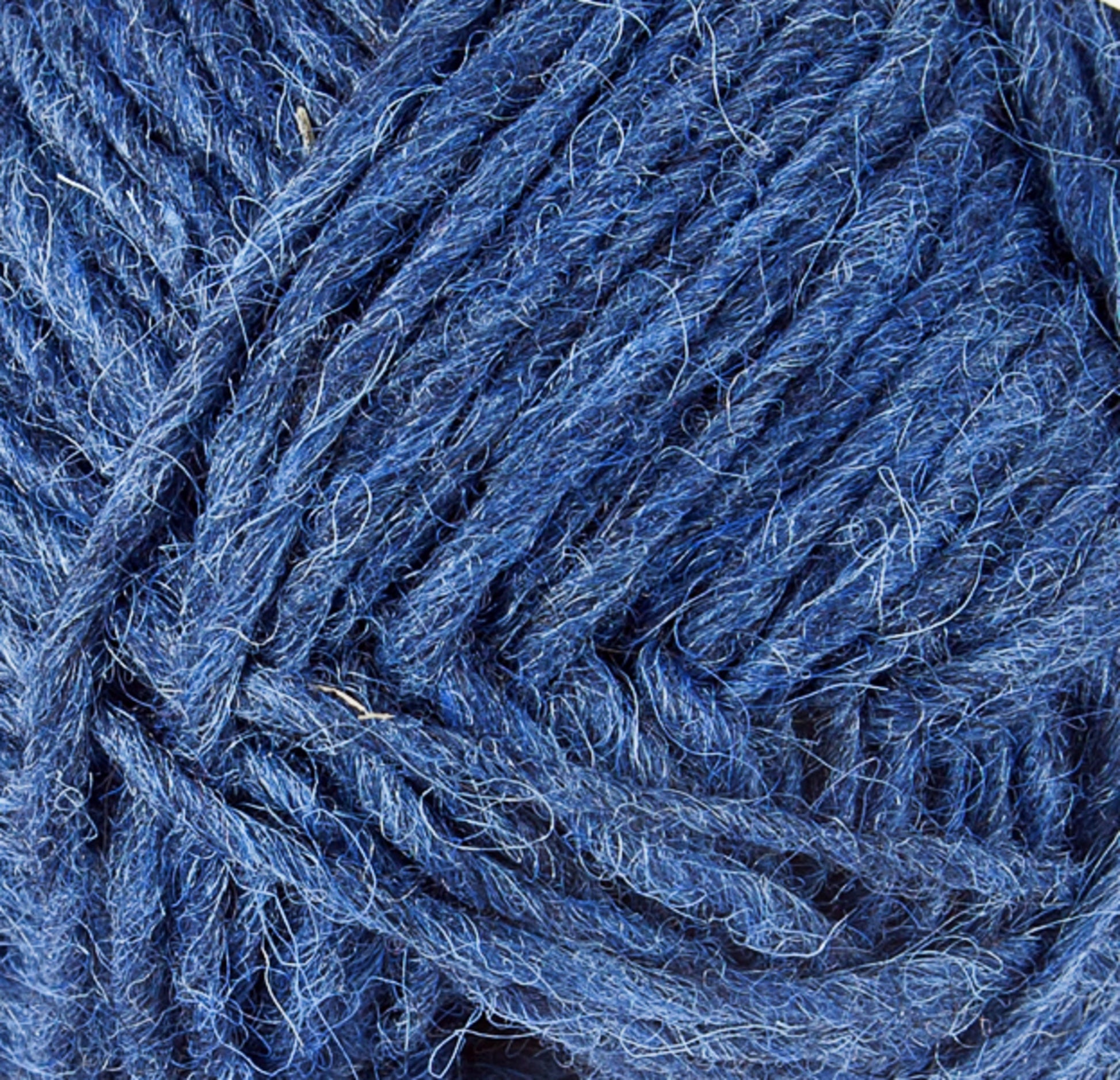 A close-up of a ball of Berroco, Inc.'s Léttlopi (Lite Lopi) Icelandic Wool Yarn. The fibers are thick and intertwined, showcasing a variety of blue tones that range from light to dark. The texture appears soft and slightly fuzzy, with some loose strands visible, making it perfect for creating durable garments with intricate colorwork knitting designs.