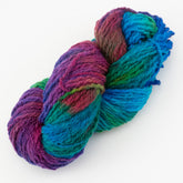 A skein of **Great Adirondack Galloway** hand-dyed variegated yarn from **Great Adirondack Yarn Co, Inc.**, featuring colors that range from deep purple and blue to green and red, twisted together against a white background. The yarn appears soft and thick, suggesting it's ideal for knitting or crocheting cozy merino accessories.