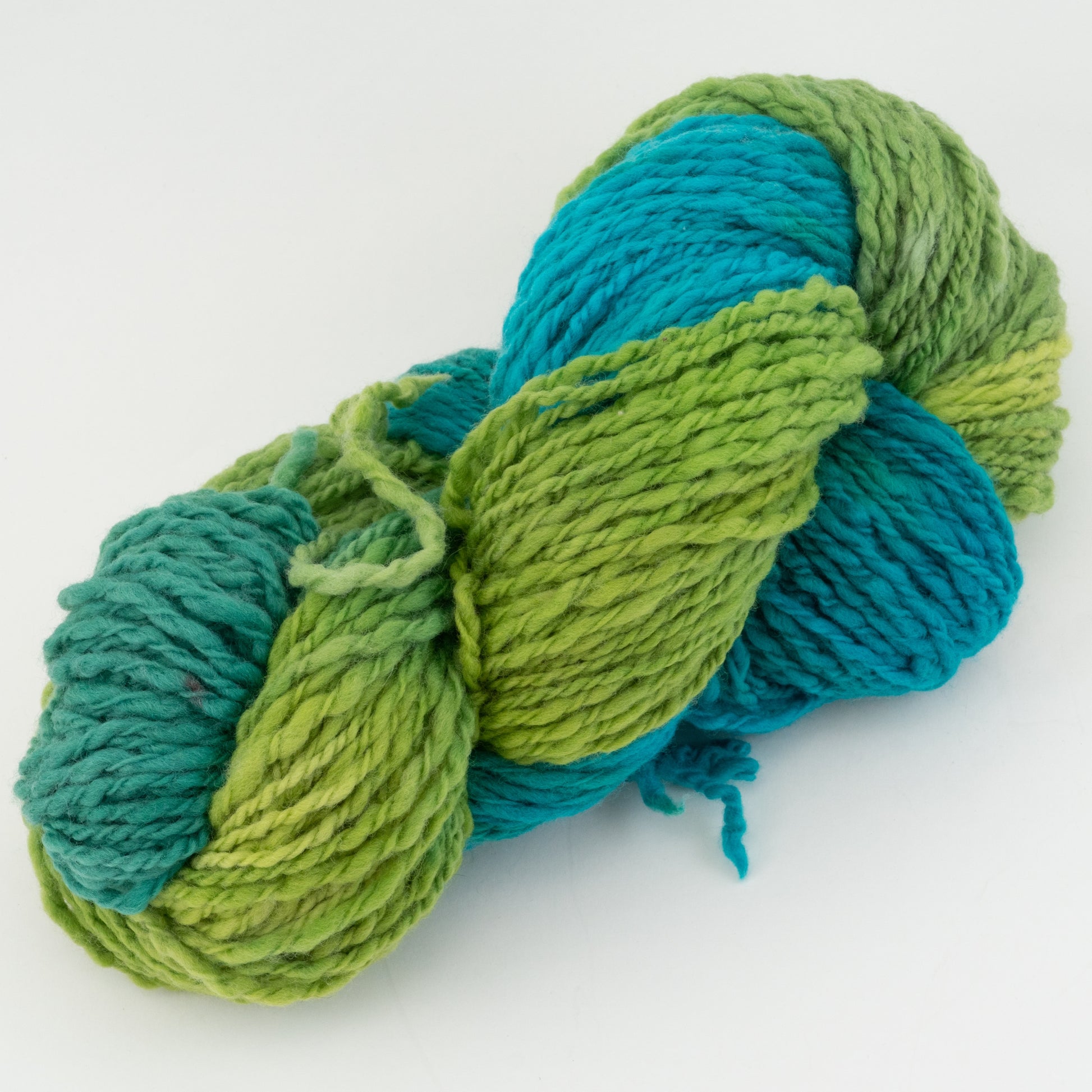 A skein of Great Adirondack Galloway yarn from Great Adirondack Yarn Co, Inc., featuring a hand-spun, hand-dyed blend of vibrant green and turquoise colors, twisted into a coil and set against a plain white background. The plush and slightly textured yarn is ideal for crafting unique accessories.