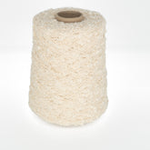 A cylindrical spool of Henry's Attic Cathy - Cotton Yarn in a cream color is standing upright against a white background. The yarn features a bumpy, curly texture, resembling boucle or a similar type, ideal for crafting intricate lace patterns with varying textures when knitting or weaving.