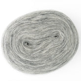 A close-up photo captures a coiled oval-shaped skein of Berroco, Inc.'s Plötulopi Unspun Icelandic Wool Yarn in light gray. The image highlights the yarn's soft and fuzzy texture, with slight variations in shade that lend it a subtle, marbled appearance. The unspun yarn coil is set against a plain white background.