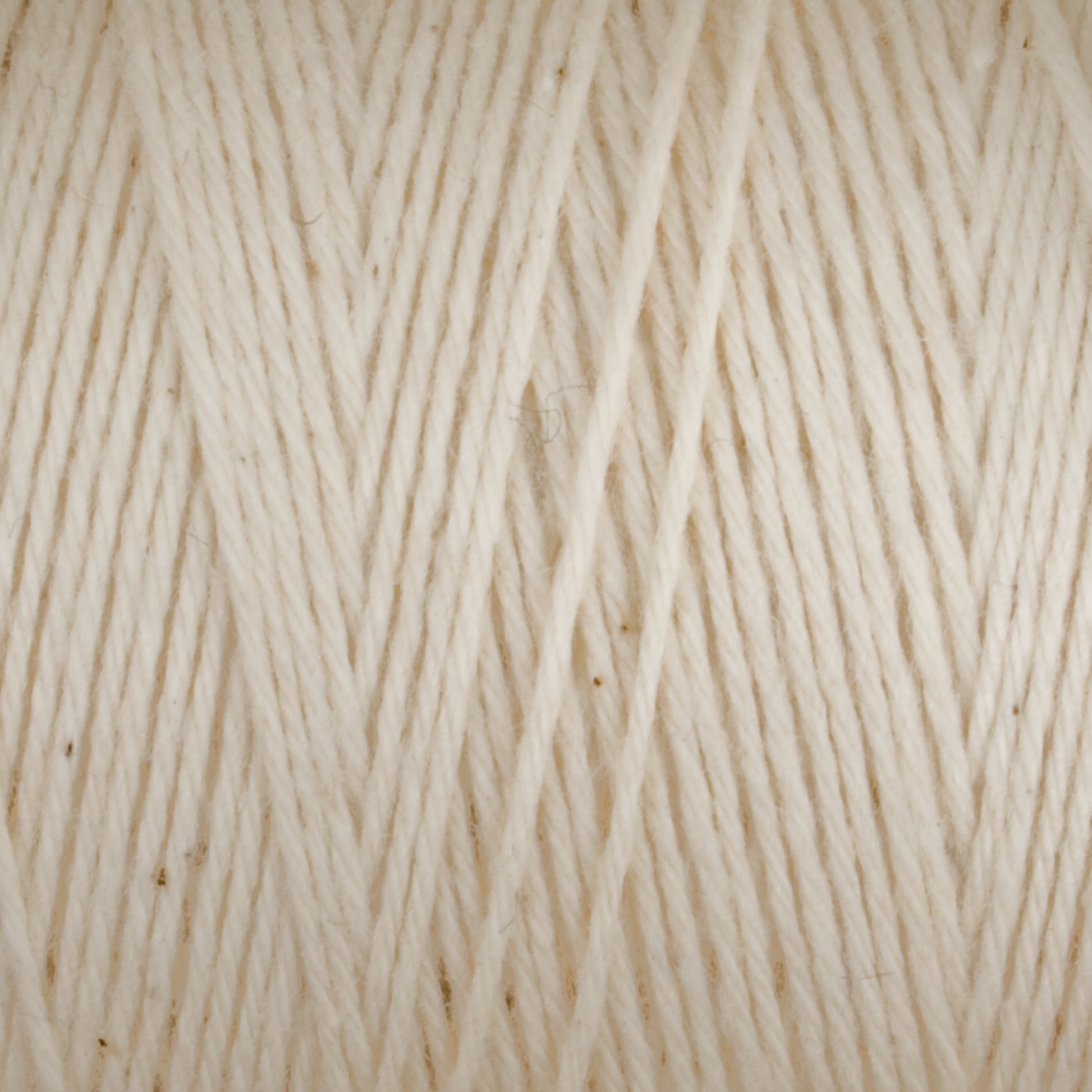 Close-up of a ball of Great Northern Weaving's Cotton Carpet Warp 8/4. The texture, reminiscent of traditional cotton warp yarn, is clearly visible, showcasing its fibrous, slightly fuzzy characteristics. The strands are wound tightly together, creating a neat, orderly pattern with small, scattered flecks of darker fibers.