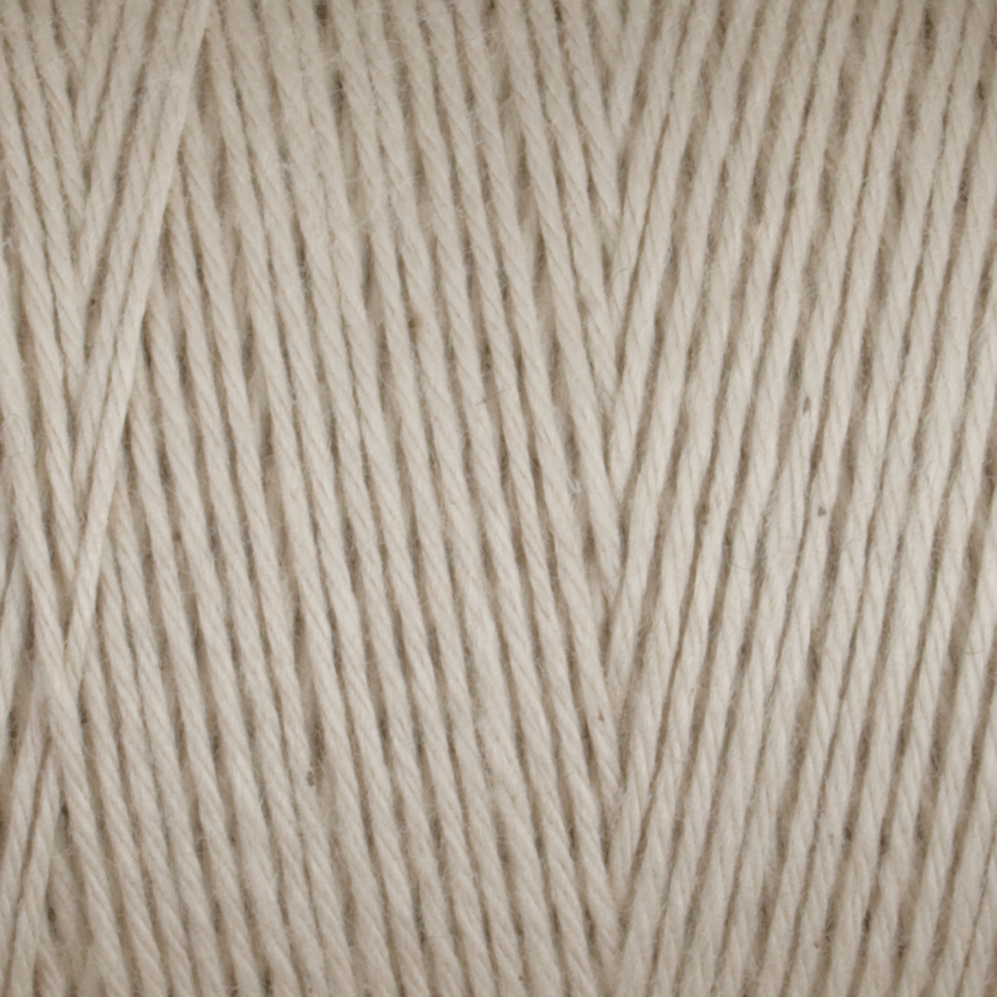 Close-up image of Great Northern Weaving’s Cotton Carpet Warp 8/4 in beige. The detailed texture reveals tightly spun fibers with a slightly uneven, natural look. The color is a soft, neutral beige with subtle tonal variations, providing a warm and cozy feel ideal for knitting or crocheting projects such as cozy coverlets.