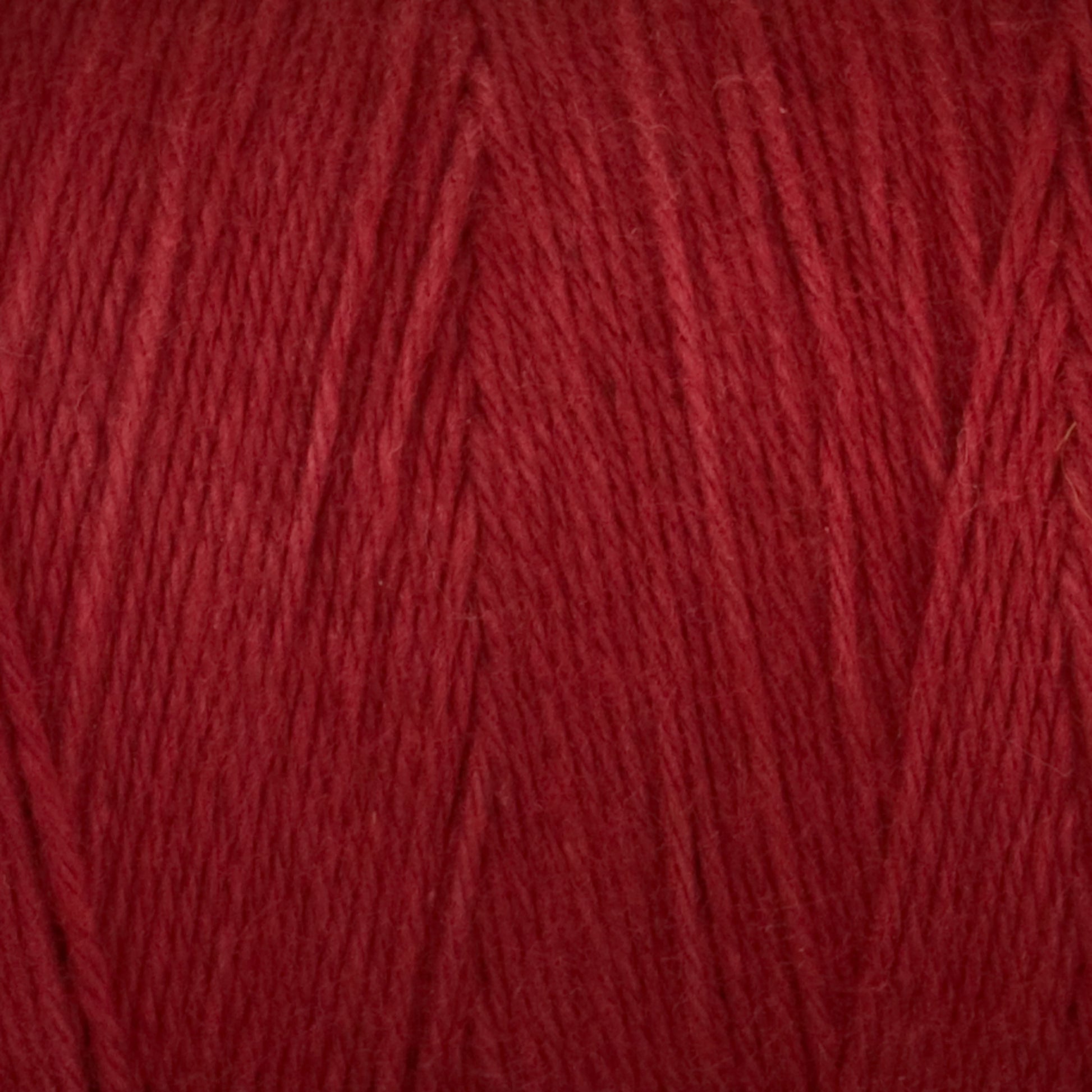 A close-up image of Great Northern Weaving's Cotton Carpet Warp 8/4. The yarn's texture is clearly visible, showcasing fine threads tightly spun together. The rich red color is uniform throughout, highlighting the softness and quality of this cotton warp yarn often used in coverlets.