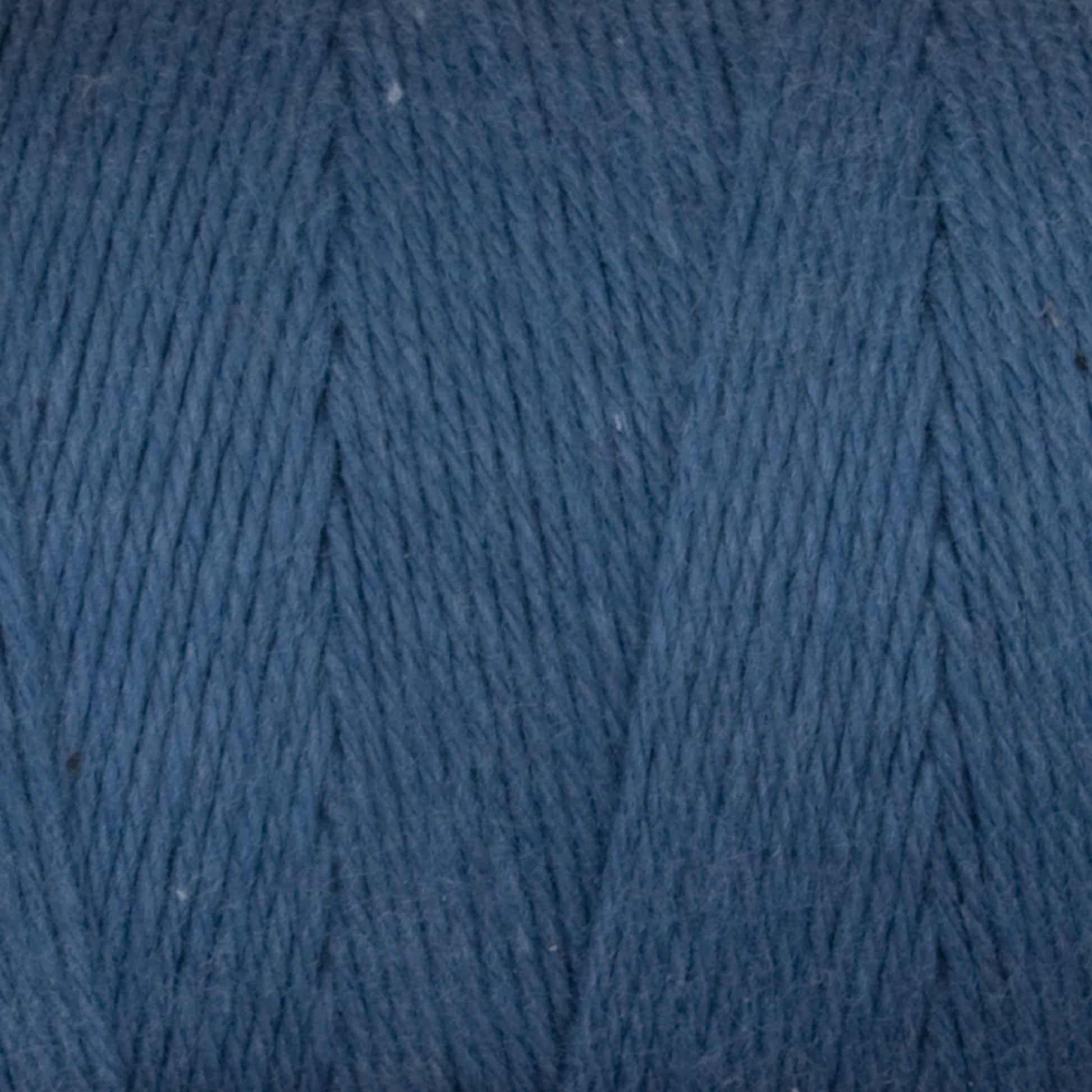 Close-up view of a spool of Great Northern Weaving's Cotton Carpet Warp 8/4 in blue. The image highlights the texture and fibers, showing the tight, even strands wound closely together. The yarn has a soft and slightly fuzzy appearance, perfect for weaving intricate coverlets or sturdy rag rugs.