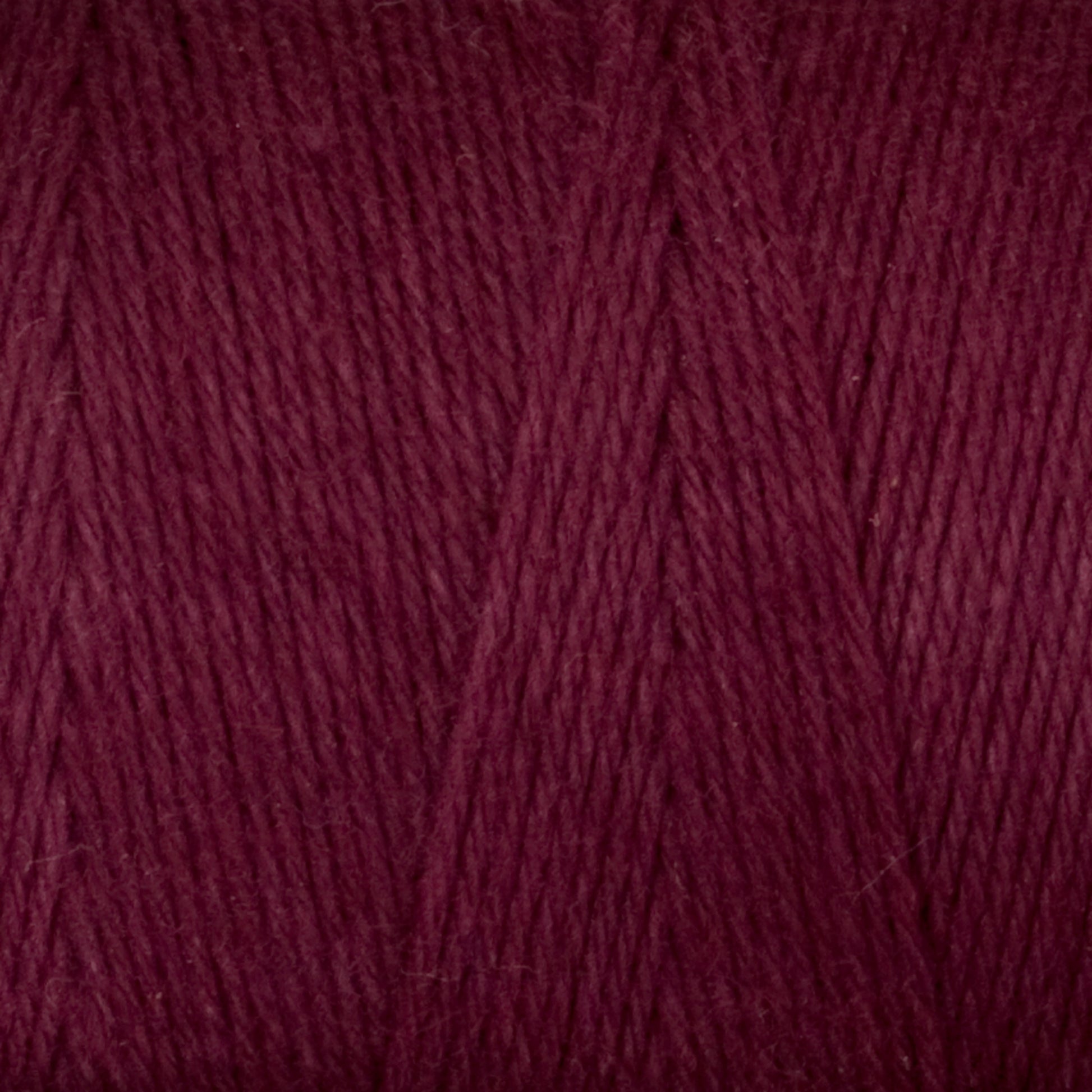 A close-up view of Great Northern Weaving's Cotton Carpet Warp 8/4 yarn, often used in rag rugs. The texture is soft and slightly fuzzy, with individual strands twisted together, creating a uniform and tightly knit pattern. The rich, deep maroon color is consistent throughout the yarn.