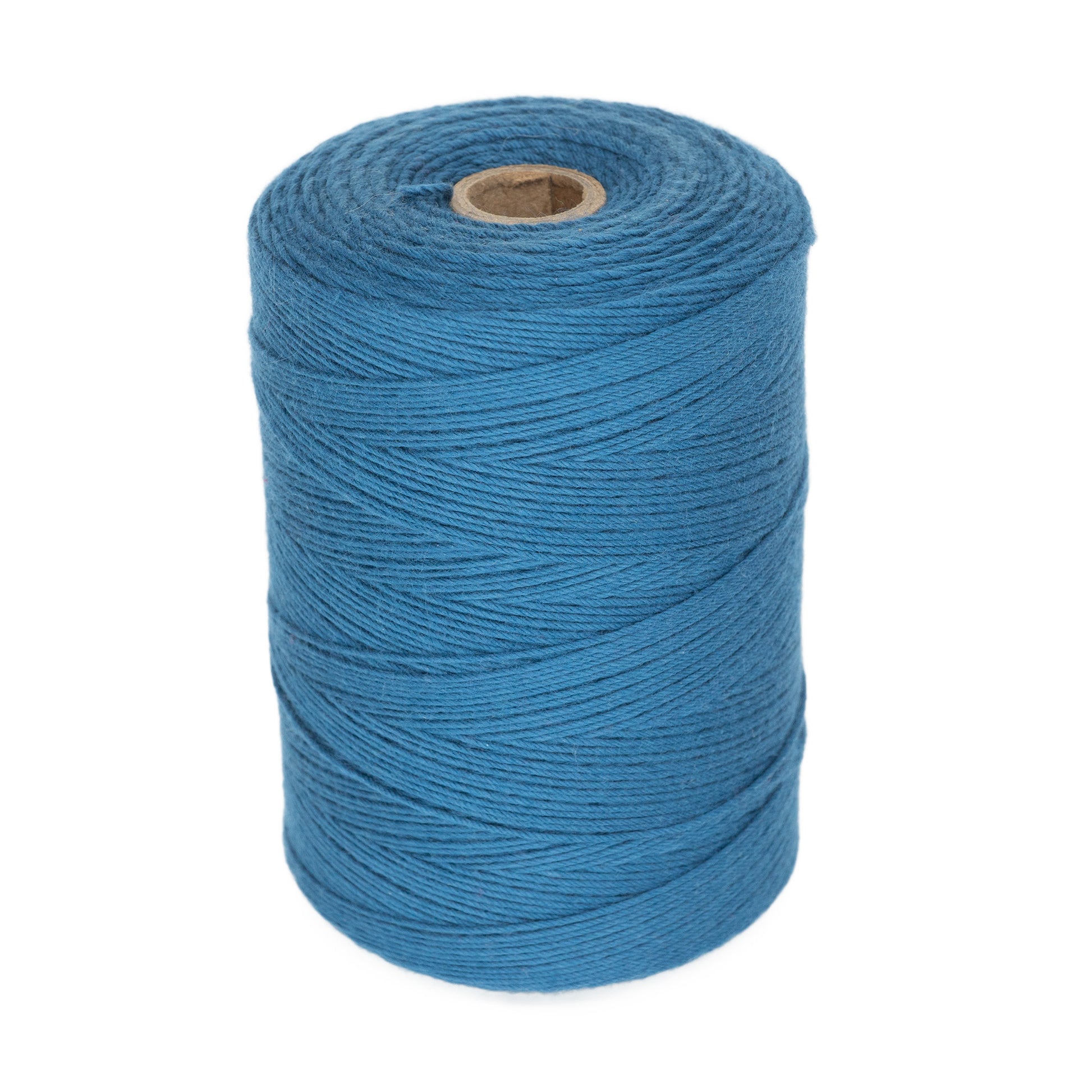 A large spool of Great Northern Weaving's Cotton Carpet Warp 8/4 in blue, perfect for creating rag rugs or coverlets, stands upright. The tightly wound cotton warp yarn encircles a cylindrical cardboard core. The consistent blue color indicates the spool is full and unused. The background is white, highlighting its pristine condition.