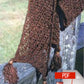 An elegant, brown, tasselled Chainette Scarf from Halcyon Yarn, showcasing a diagonal openwork pattern, is draped over a wooden fence. In the lower right corner, there’s an icon featuring a PDF symbol and an Adobe logo, indicating a downloadable document. The background captures an outdoor scene with blurred grass.