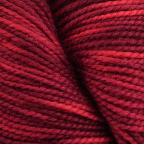 A close-up image of tightly wound Happy Feet Sock Yarn by Plymouth Yarn Co., featuring rich shades of red and maroon. The texture is soft and slightly fuzzy, with subtle variations in color highlighting the twists and turns of the superwash Merino wool fibers.