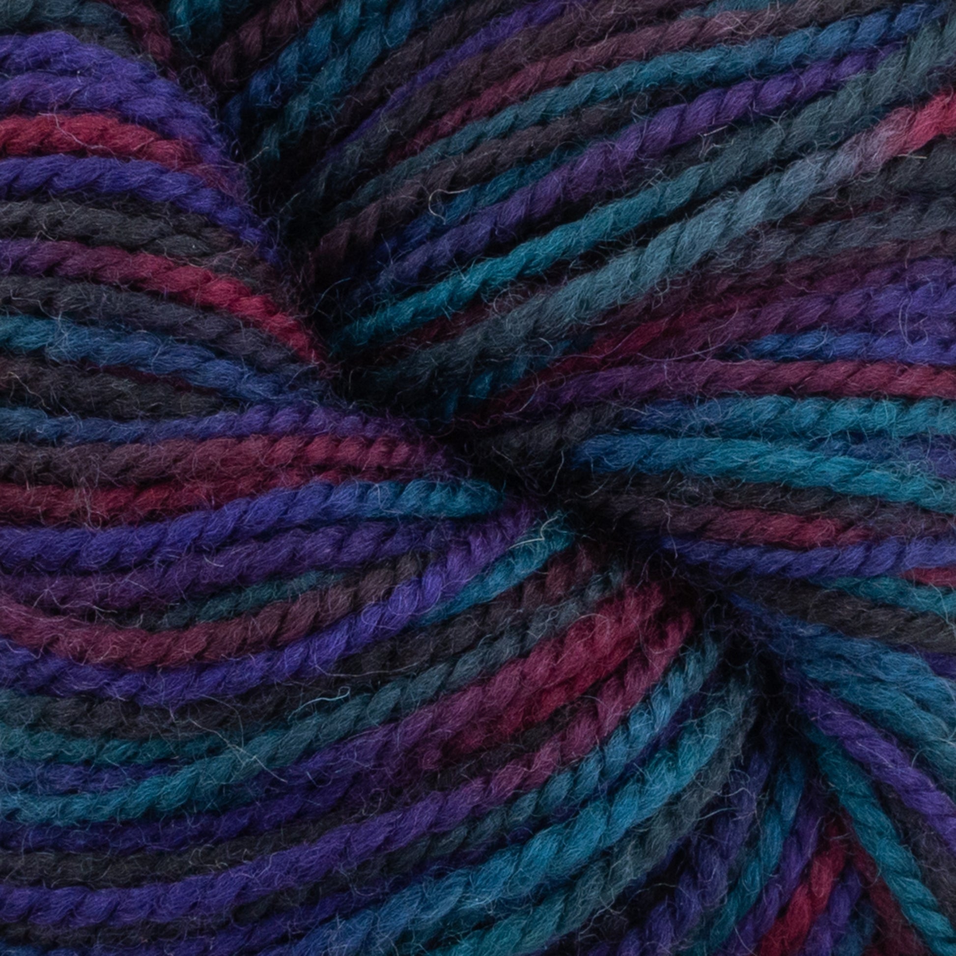 Close-up of multicolored yarn, featuring deep shades of red, purple, blue, teal, and black. The tightly wound strands of Plymouth Yarn Co.'s Happy Feet Sock Yarn have a soft, woolen texture and showcase a rich gradient of colors. This superwash Merino wool is perfect for durable knitting projects.