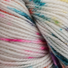 A close-up view of Happy Feet Sock Yarn showcases the superwash Merino wool yarn primarily in white, adorned with delightful speckles of vibrant colors such as pink, blue, orange, green, and purple. This artistic blend from Plymouth Yarn Co. gives it a vibrant and lively appearance, making it perfect for crafting beautiful sock projects!