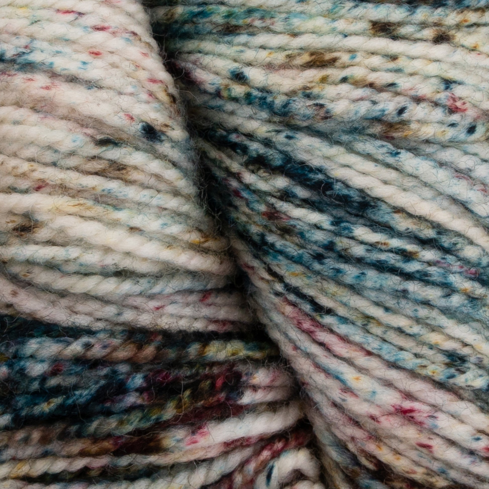 A close-up of Happy Feet Sock Yarn by Plymouth Yarn Co. reveals a soft and wooly texture, with off-white as the primary color enhanced by specks of blue, green, brown, pink, and red woven throughout the superwash Merino wool fibers—perfect for durable knitting projects.