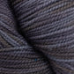 Close-up image of a skein of dark gray Happy Feet Sock Yarn by Plymouth Yarn Co. The yarn appears tightly wound and textured, featuring varying shades of gray with hints of interwoven blue threads. The surface showcases a mix of light and shadow, emphasizing the fibrous texture of this durable knitting yarn made from superwash Merino wool.