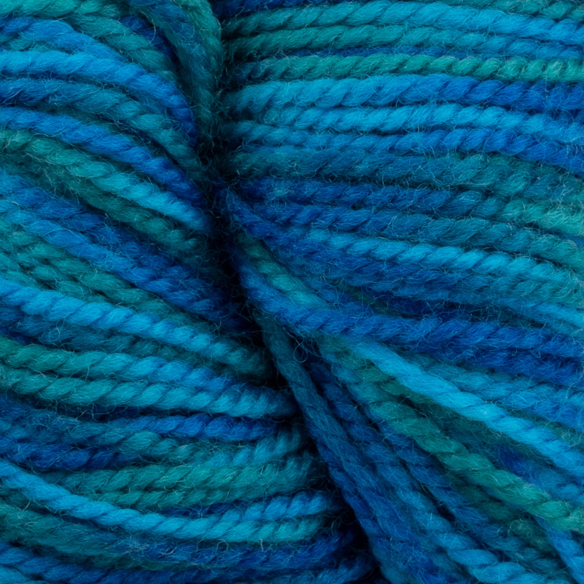 Close-up photo of soft, thick Happy Feet Sock Yarn from Plymouth Yarn Co. in various shades of blue and green, arranged to showcase the twisted texture. The superwash Merino wool colors blend smoothly from teal to deep blue, highlighting the fibers and giving a cozy, vibrant appearance.