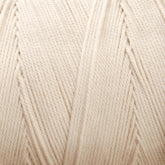 Close-up view of a tightly wound, cream-colored spool of Glimakra's Swedish Cotton Warp (Seine Twine, Fiskgarn). The texture of the fibers is visible, showcasing the intricate pattern of the cotton warp yarns' strands. The yarn appears smooth and evenly wound around the spool.