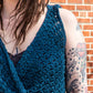 A person with dreadlocks wearing the Halcyon Yarn Ultra Twist Broomstick Lace Crochet Top stands against a brick wall. The person's arm features a tattoo of a heart with a banner reading "Mom" and decorative elements around it, and the top’s intricate crochet pattern, including broomstick lace accents, is visible.