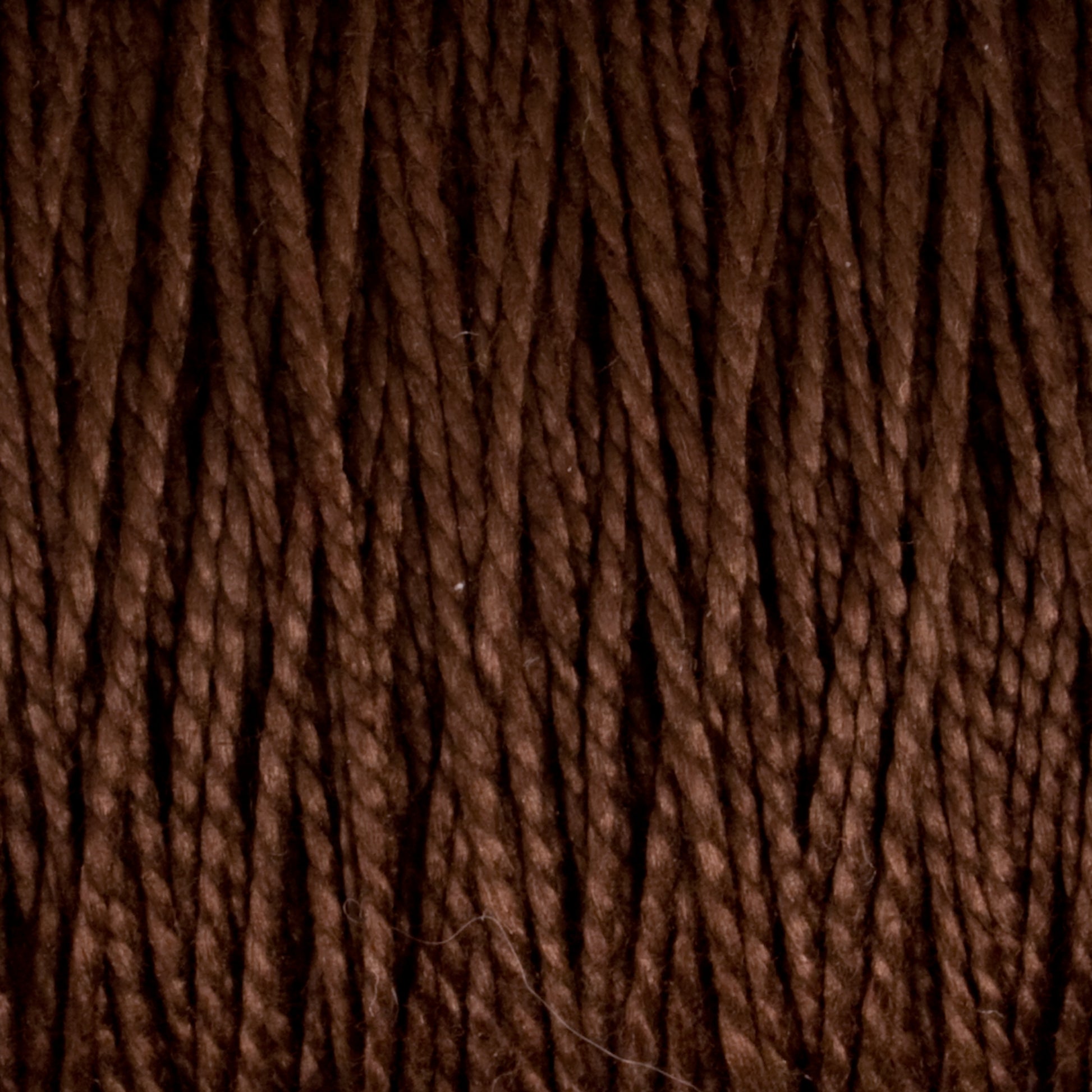 Close-up view of tightly coiled dark brown strands from Supreme Corp’s 3/2 Pearl Cotton Yarn | Mini-cone, showcasing a textured and rich fiber pattern. This versatile yarn is densely woven, creating a uniform appearance with subtle highlights and shadows.