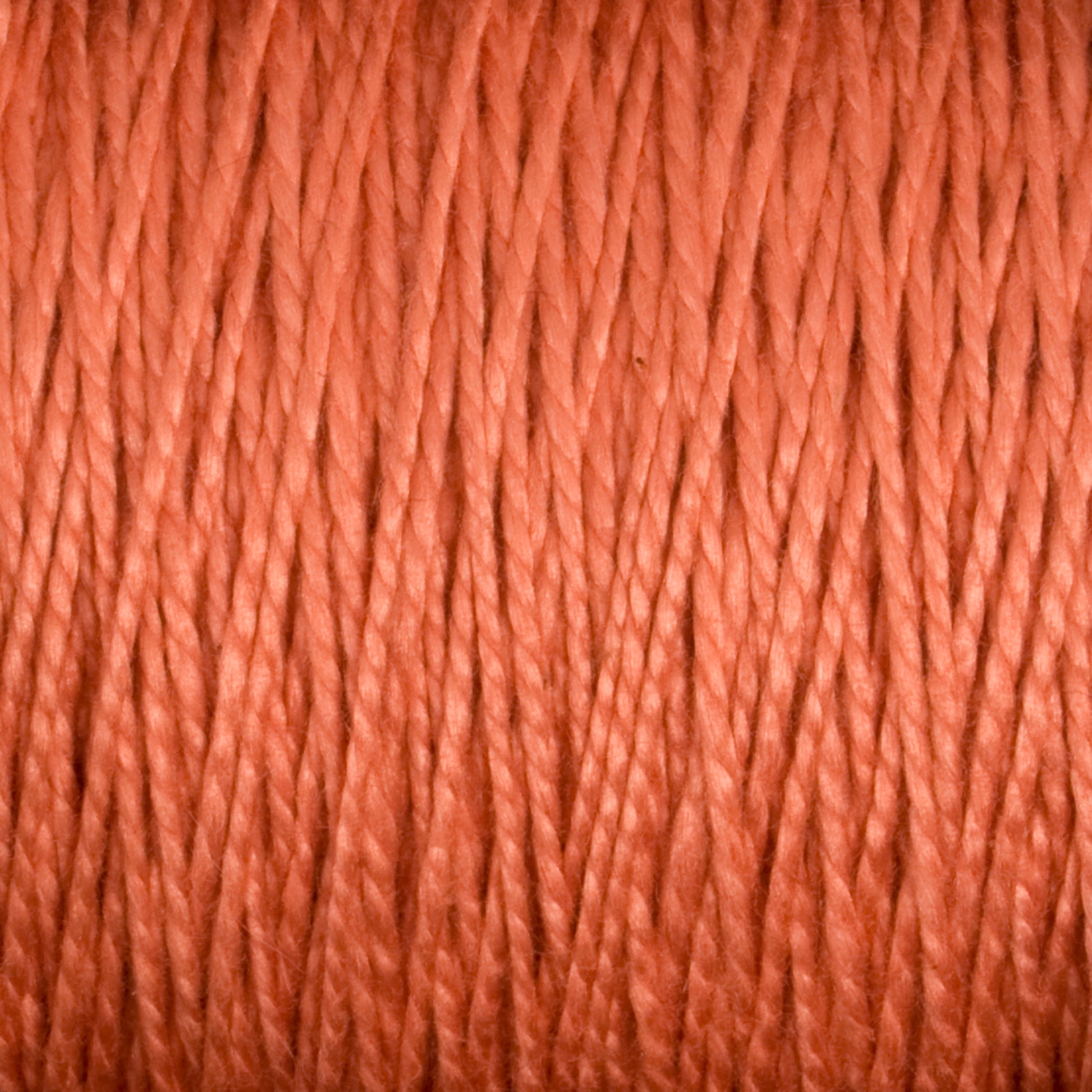 Close-up of tightly wound, coral-colored 3/2 Pearl Cotton Yarn by Supreme Corp. The strands are twisted together, creating a uniform, textured pattern across the image. The hue is a warm blend of pink and orange tones.